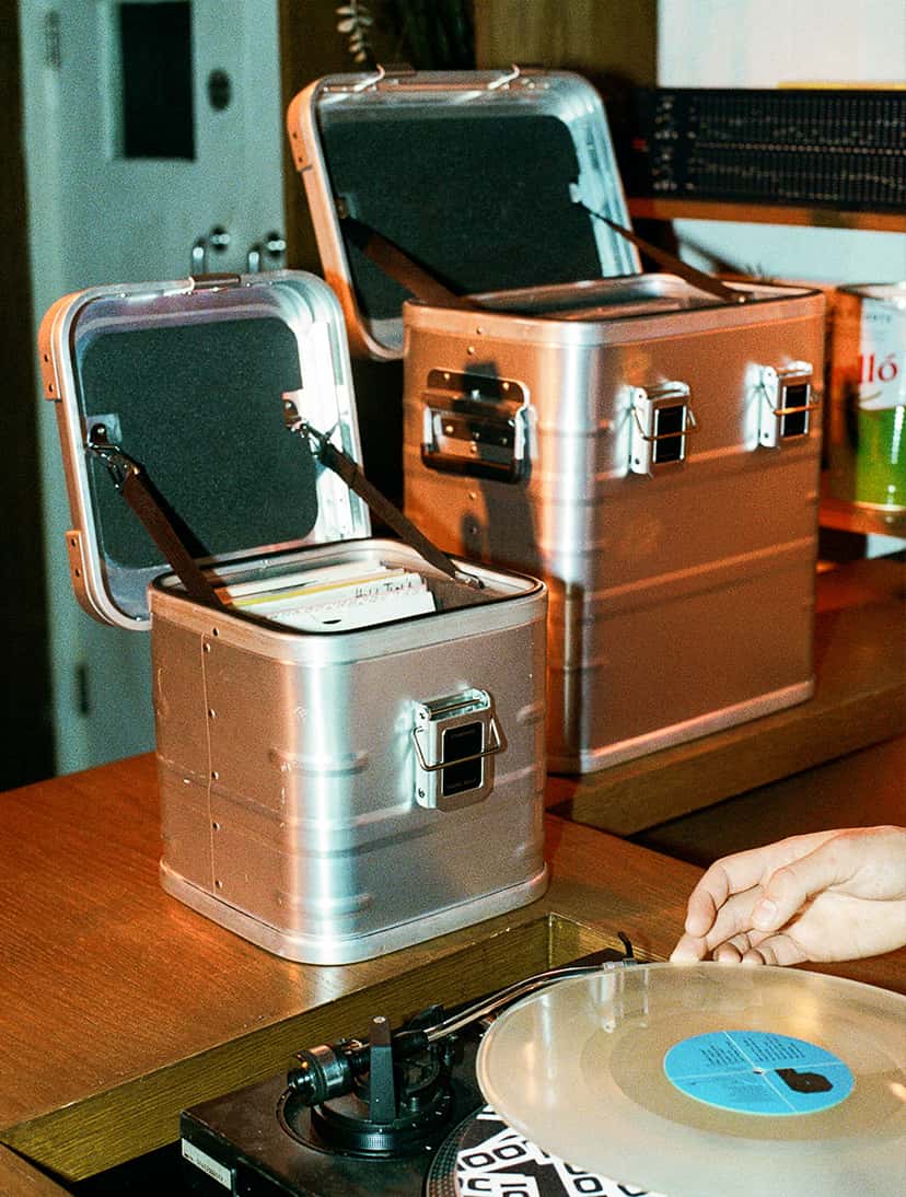 Travel Heavy 7" and 12" record cases open on a DJ booth beside a turntable