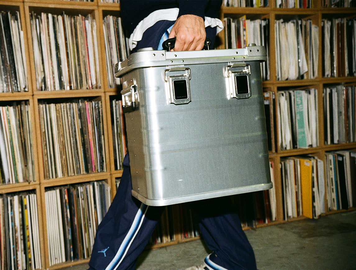 DJ carrying a Travel Heavy aluminium record case past shelves of vinyl