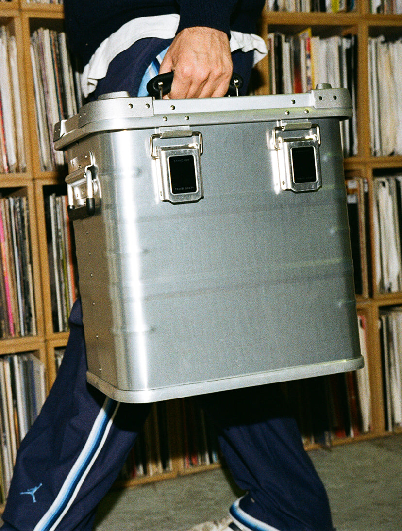 DJ carrying a Travel Heavy aluminium record case past shelves of vinyl